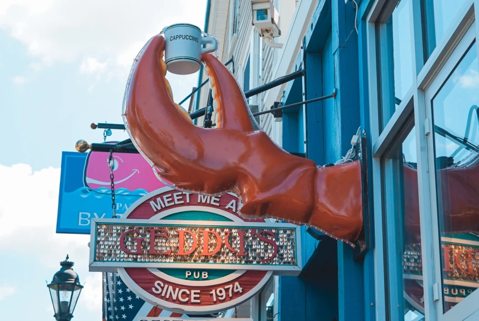 row of seaside town restaurants, with colorful signs including a lobster claw holding a tea cup 