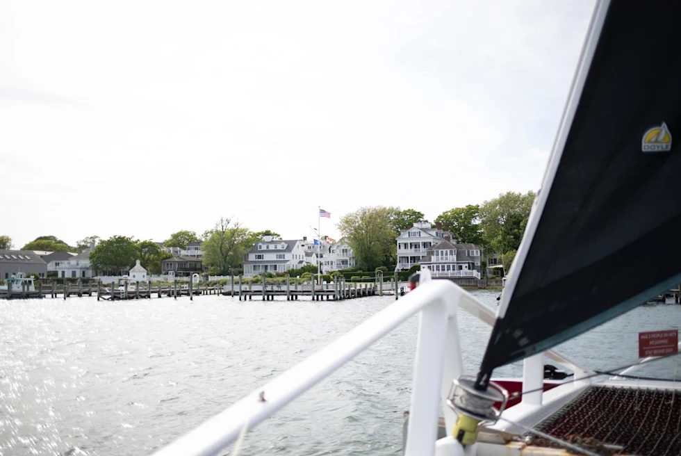 view from on a sailboat of the shore with white houses with docks and american flag waving