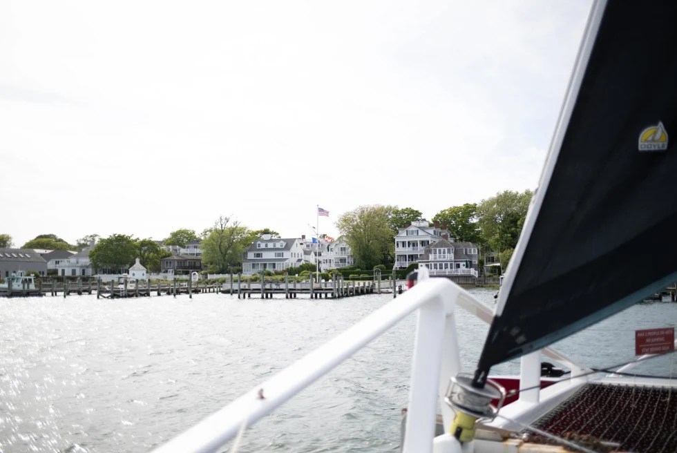 view from on a sailboat of the shore with white houses with docks and american flag waving 