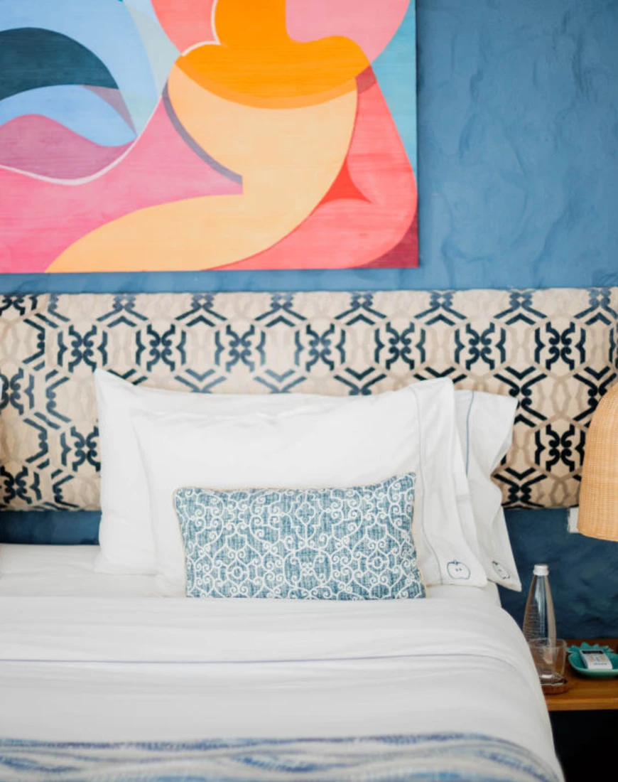 bed against a blue wall with a colorful painting