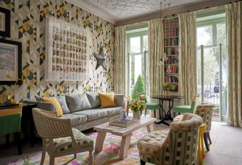 a vibrant living room with funky wallpaper and tall windows flanked by pretty drapes
