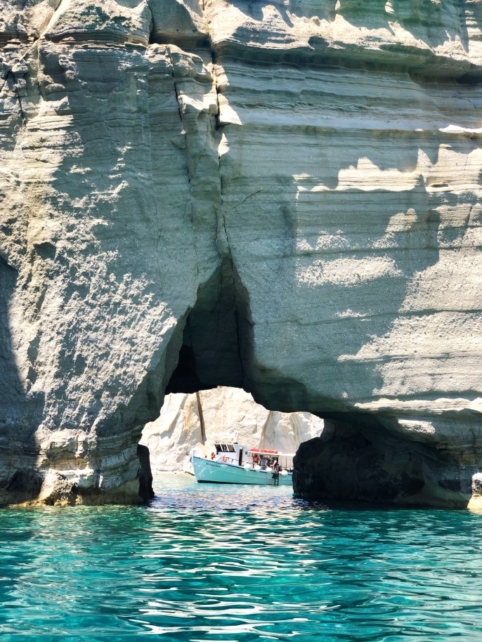 Rock formation over body of water with white boat in the distance