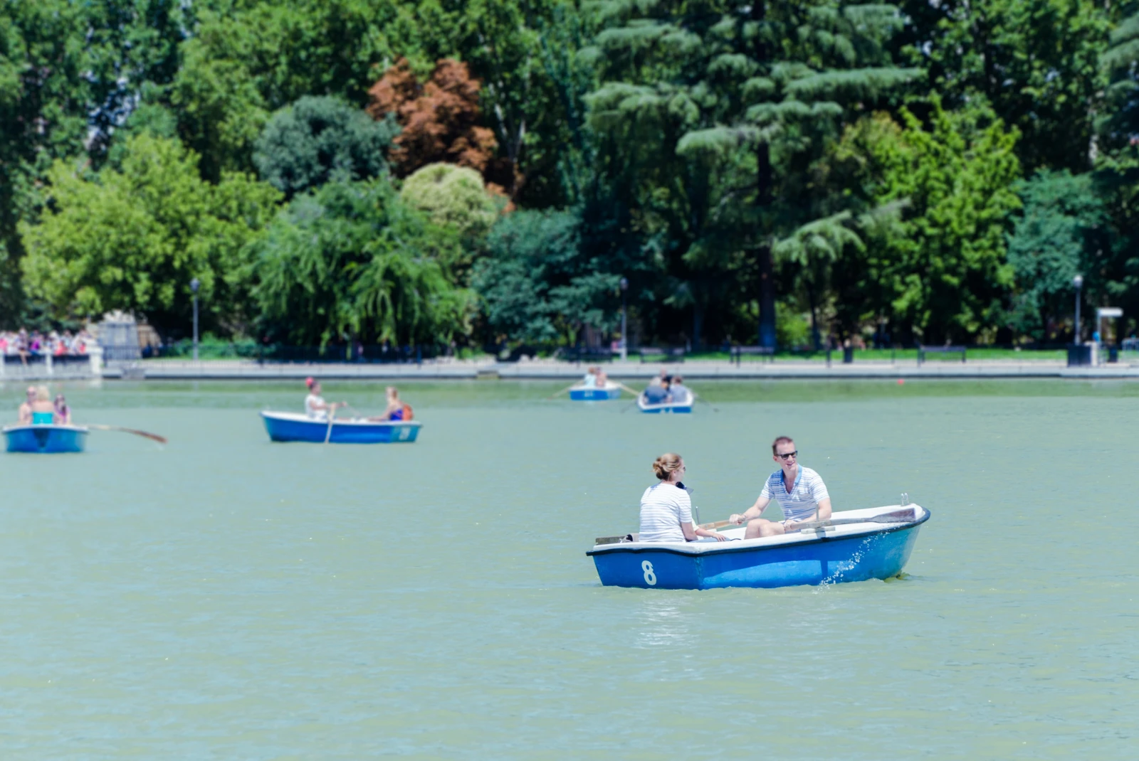 El Retiro Park in Madrid with five boats with couples in them on a lake.