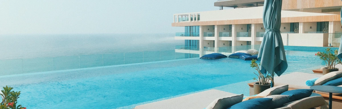 Infinity pool overlooking the ocean at a contemporary resort with lounge chairs in the foreground.