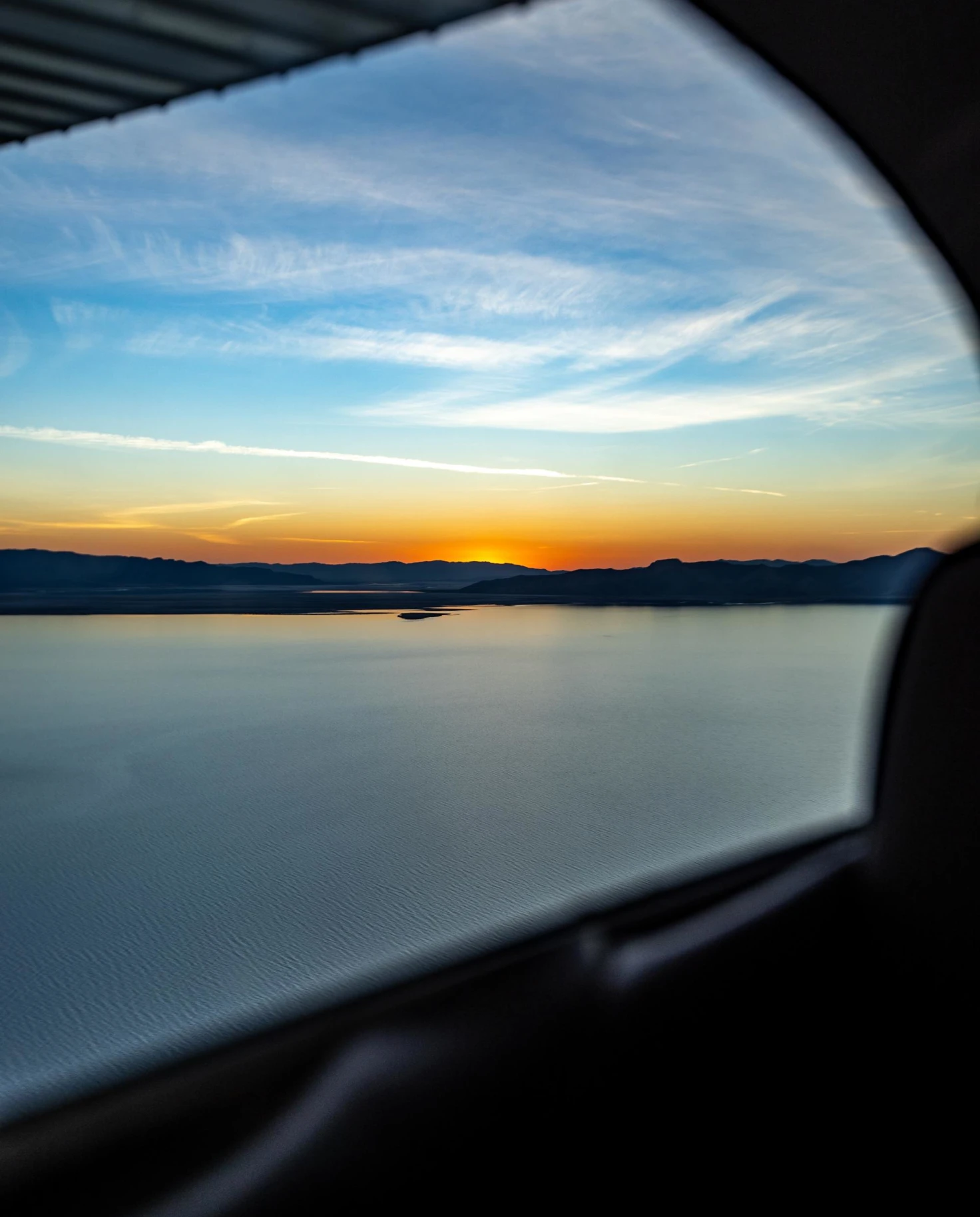 sunset over a pristine lake from the view of a car window