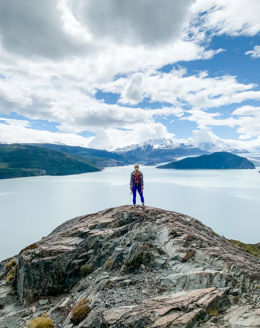 a woman stands on a rocky cliff overlooking a lake