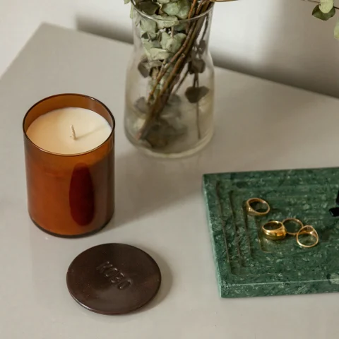 The image presents a still-life arrangement with a candle, eucalyptus branches, and a green book with rings on a light surface at a spa in Aspen.