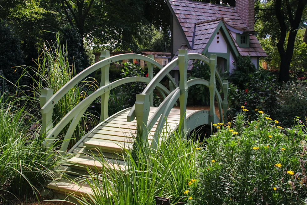 Green bridge surrounded by plants with a house in the background during daytime