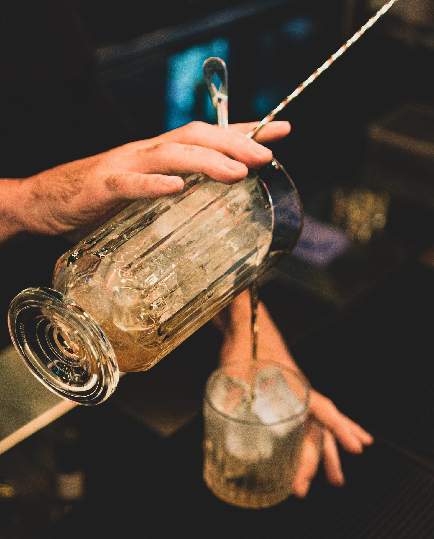 A bartender making a drink and pouring into cup. 