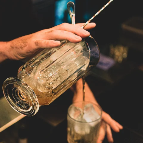 A bartender making a drink and pouring into cup. 