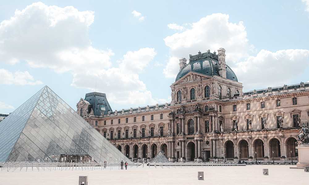 Louvre tall pointed glass structure with brown and grey building in Paris France