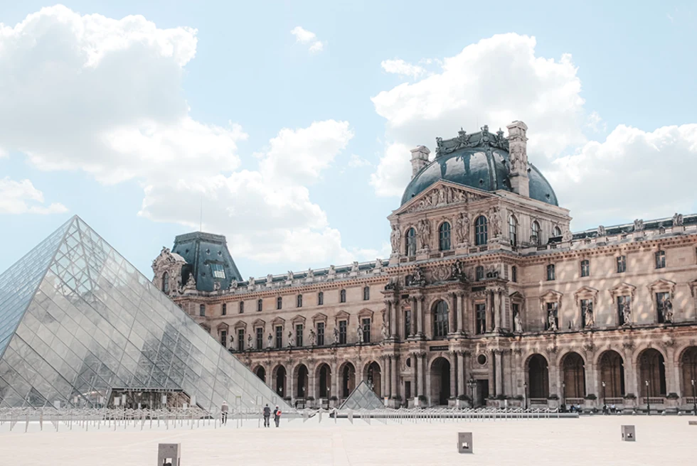 Louvre tall pointed glass structure with brown and grey building in Paris France