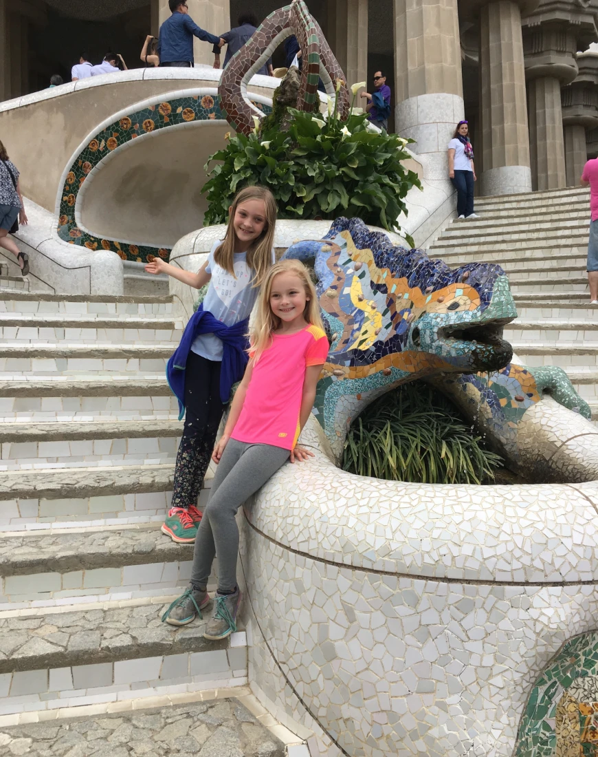 Two children posing on stone steps next to a mosaic tiled lizard water feature. 