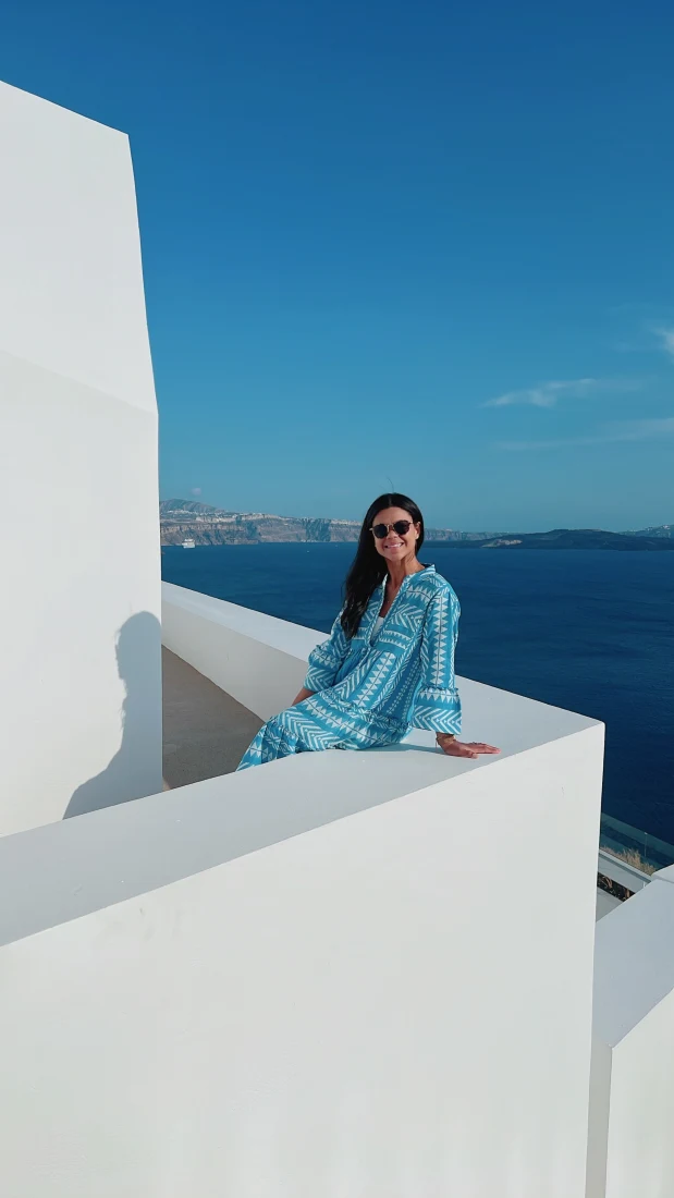 a woman in a blue dress sits on a white balcony overlooking the sea