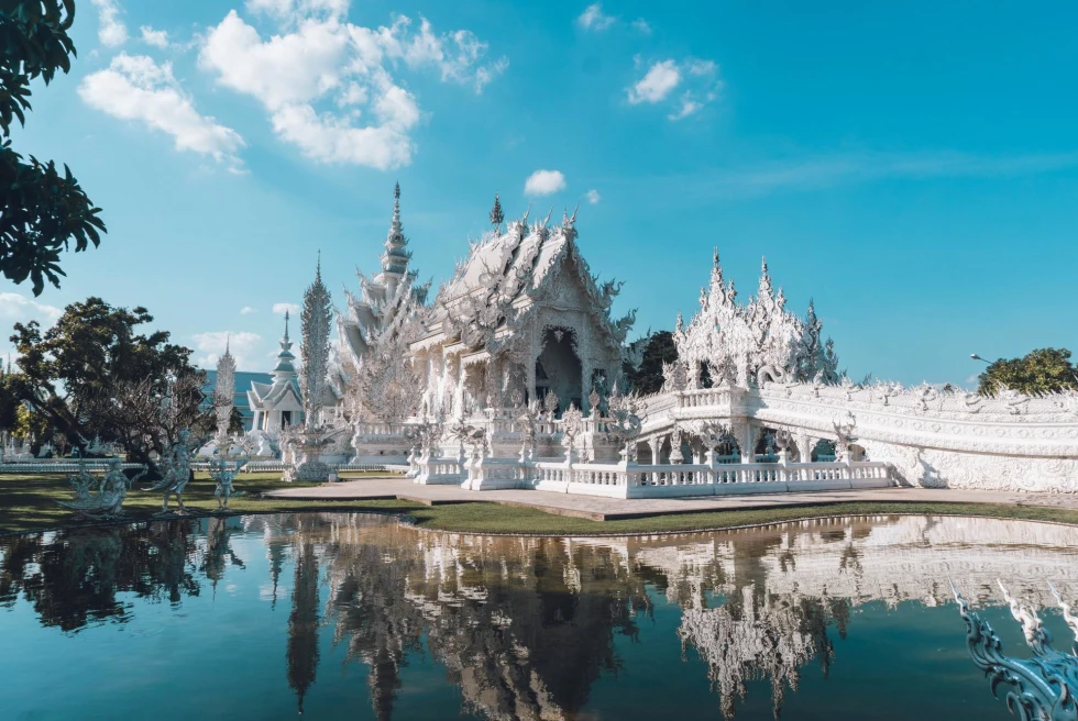 an ornate white temple and bridge with a lake on a sunny day