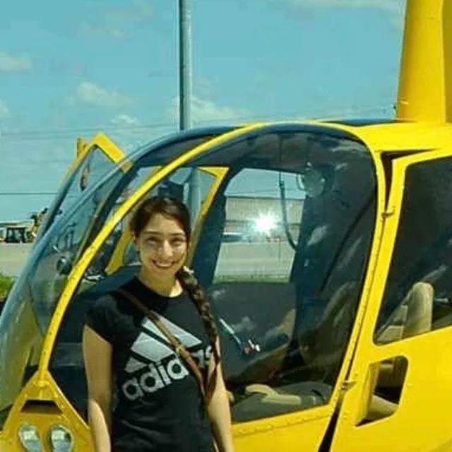 Viviana Villalobos standing in front of a yellow helicopter while wearing a black t-shirt.