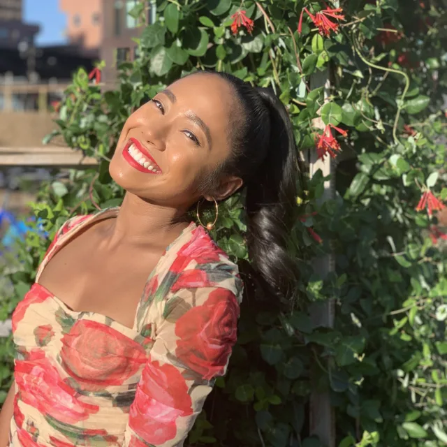 Girl wearing colorful dress standing in front of flower bush smiling at the camera