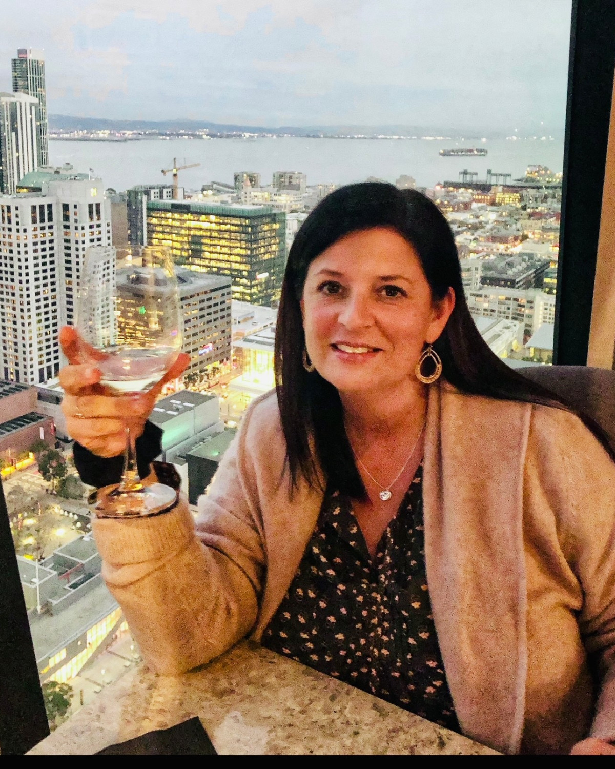 a woman holds a wine glass in a restaurant overlooking a city