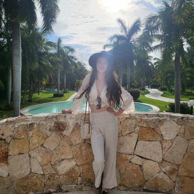 Travel Advisor Lauren Pawlowski in an all-white outfit standing outside with palm trees and the sun in the background.