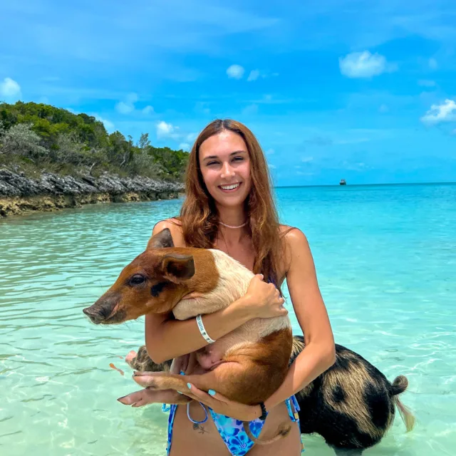 Travel Advisor Kaylee Morgan standing in blue water in the Bahamas with a pig in her arms.