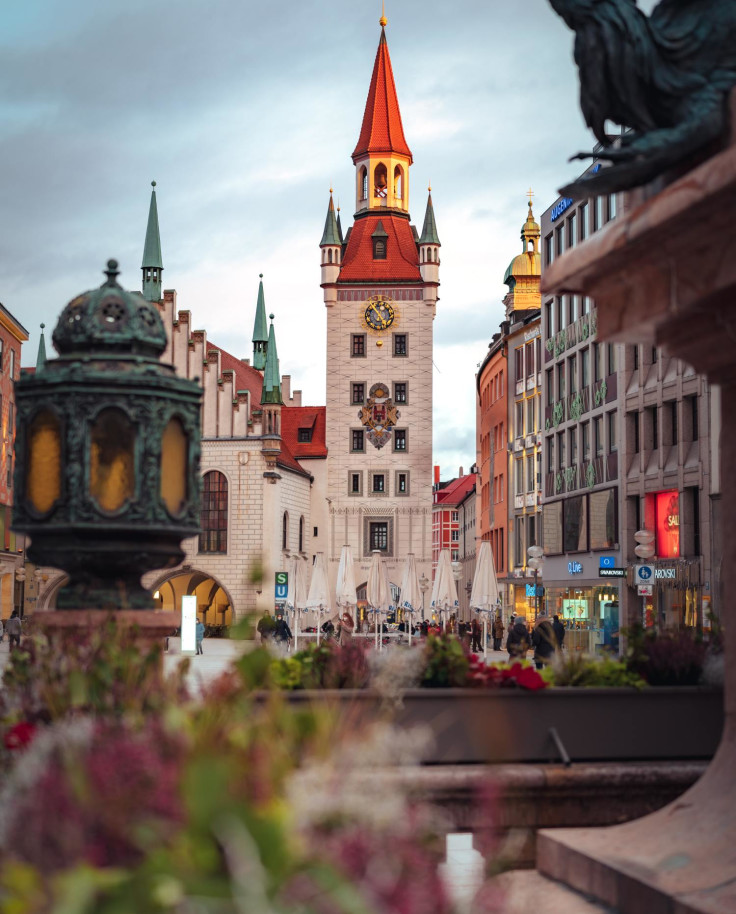 View of iconic tower in Munich from fountain on bright but cloudy day.