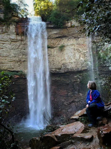 A person sitting on a rock next to a waterfall during the daytime.