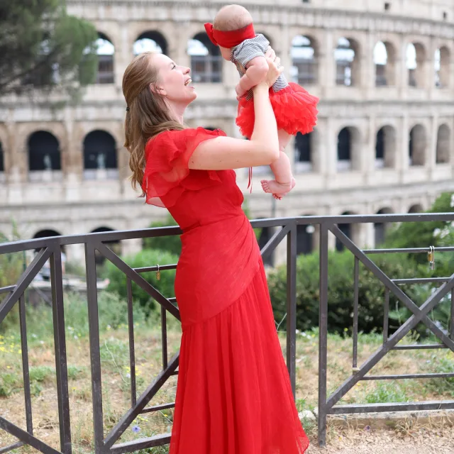 travel advisor Elle Winslow in a red dress holding her baby girl in front of the Colosseum 