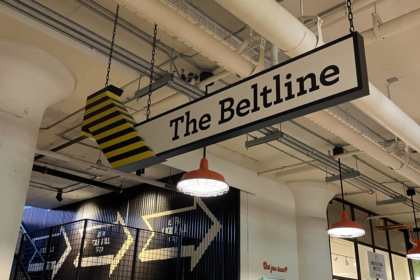 A black, yellow and white sign that reads 'The Beltline' in a building with striped walls and white industrial ceilings.