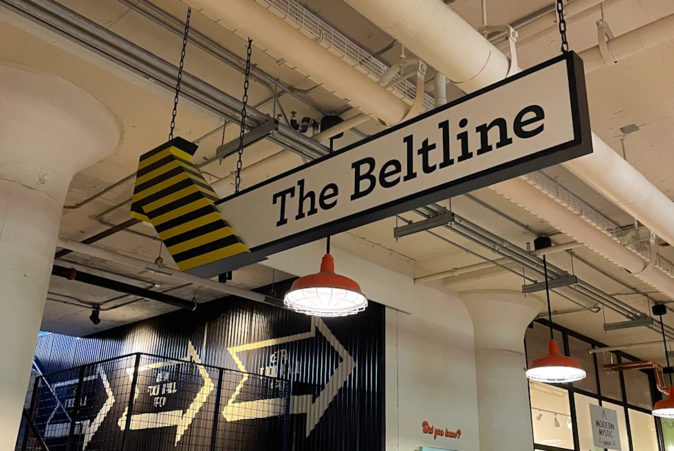 A black, yellow and white sign that reads 'The Beltline' in a building with striped walls and white industrial ceilings.