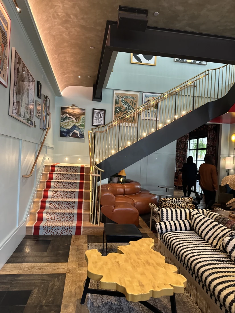 Beautiful staircase with gold bannisters and carpeted steps with artwork on the walls and a seating area by the bar with a black and white striped sofa and coffee table