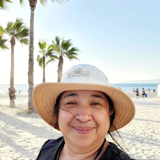 Travel advisor Gemma Datuin wears a sun hat on a white sand beach with palm trees in the background