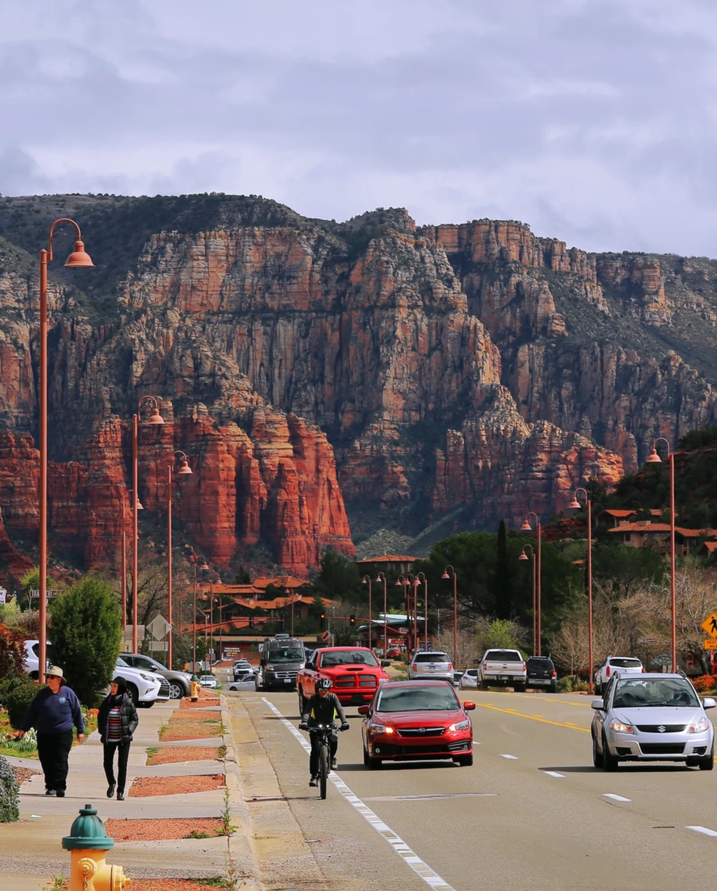 Sedona Arizona red clay mountains street with red and silver cars tall red lights and people walking and biking dressed