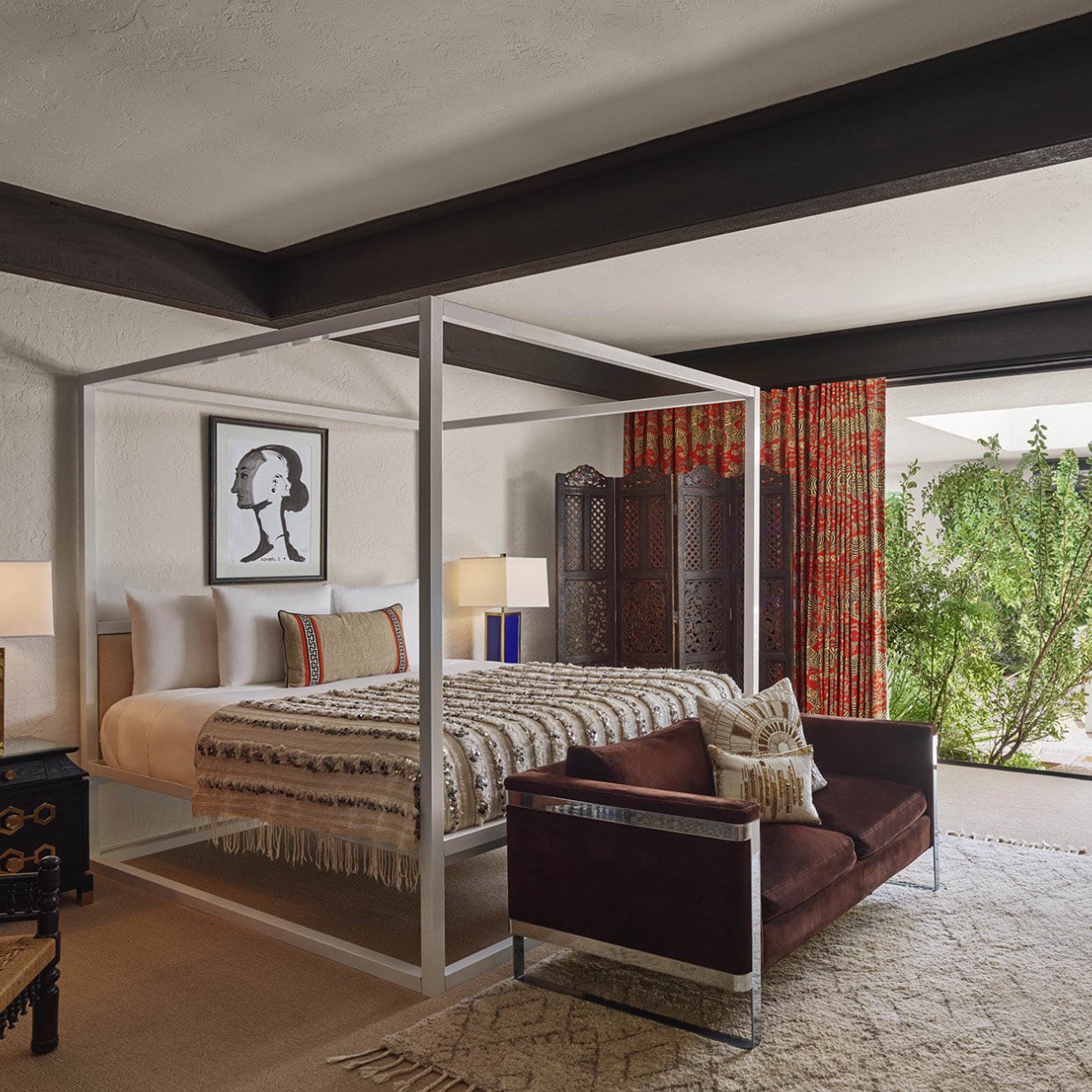 a four-post bed in a chic space with floor-to-ceiling windows leading out to a leafy deck