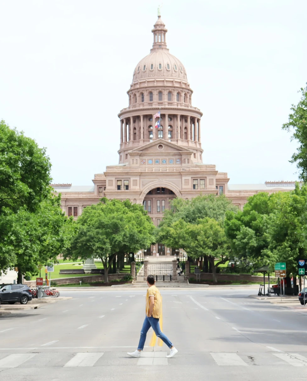 Man walks in crosswalk with capitol building in the back in Austin, Texas