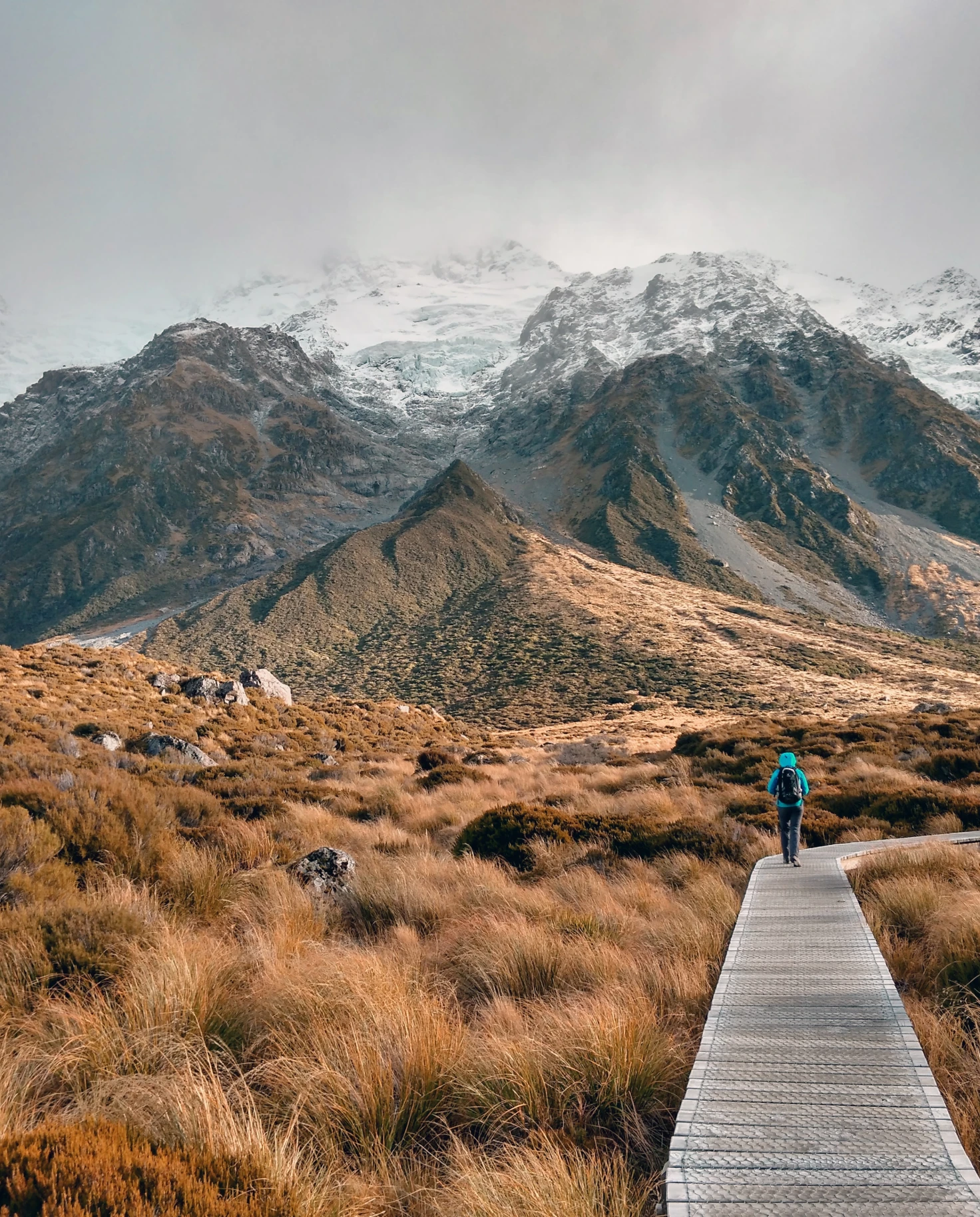 Person walking on wood path next to valley and snow-covered mountains