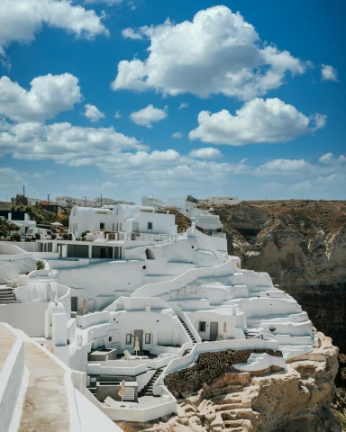 A picturesque scene of white-washed Greek buildings on a cliffside under a blue sky with clouds.