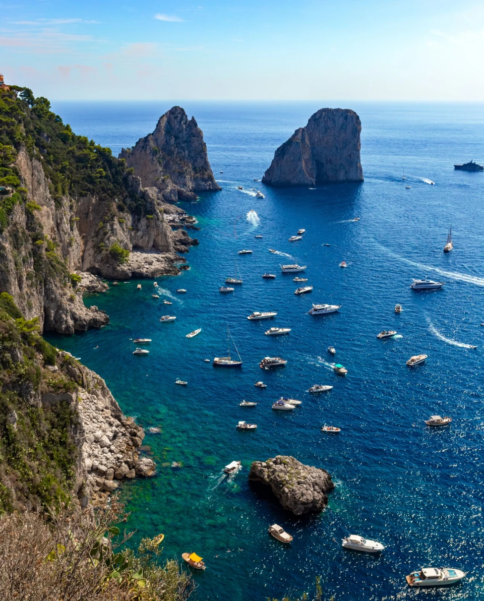 blue waters off an island with rock formations in the water and dotted with boats 