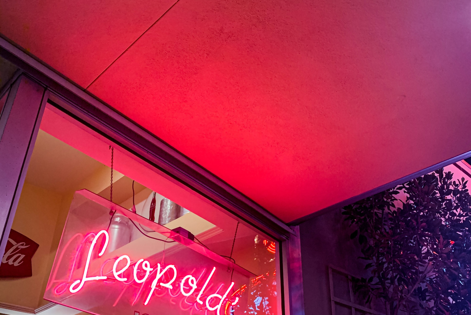 A pink neon sign that reads 'Leopold's Ice Cream' on a glass window with 20 brown wooden frames with white photographs inside, hung on a yellow wall.