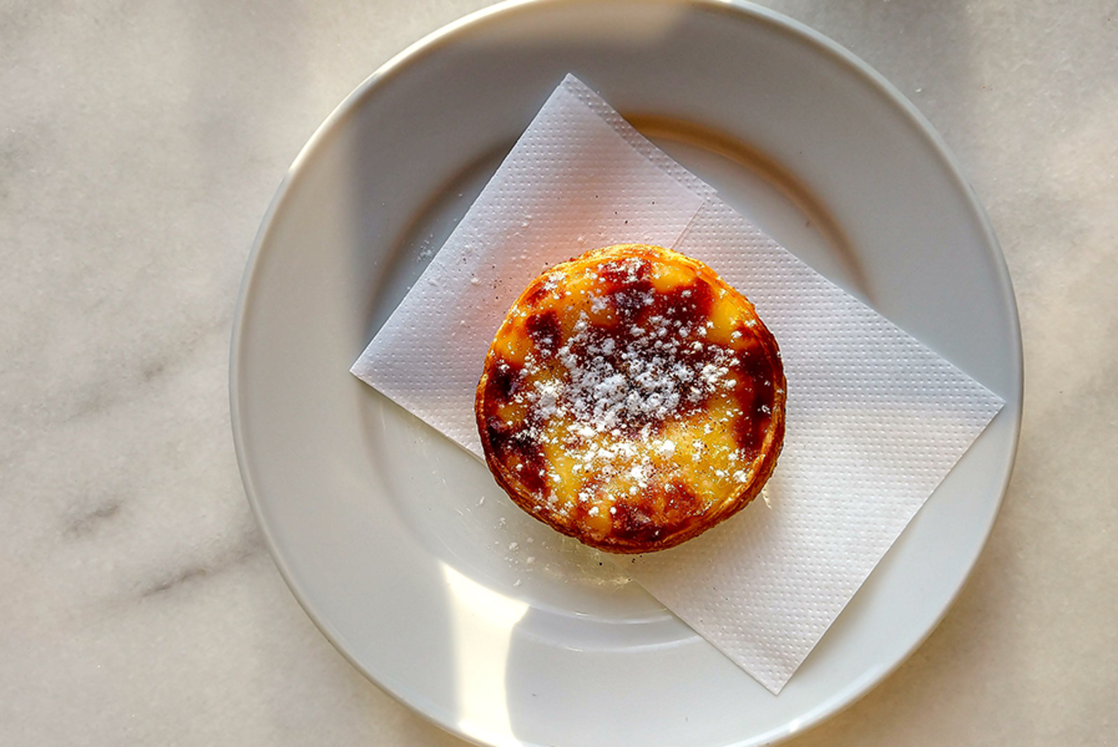 Portugal Belem pastry Pasteis de Nata with powdered sugar on a marble table white plate and napkin 