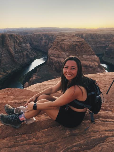 Fora travel agent Cara Zucker sitting on cliff overlooking water during sunrise