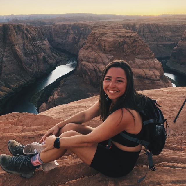Fora travel agent Cara Zucker sitting on cliff overlooking water during sunrise