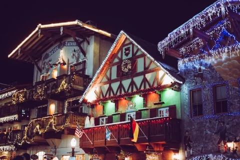 The exterior of a wooden chalet decorated with Christmas lights, an American and German flag.