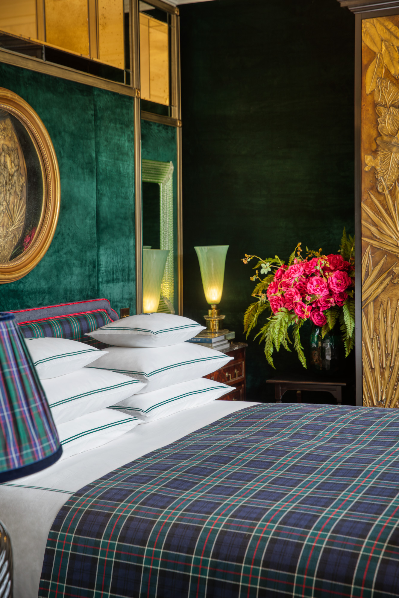 a bed with a green plaid blanket near a vase of red flowers