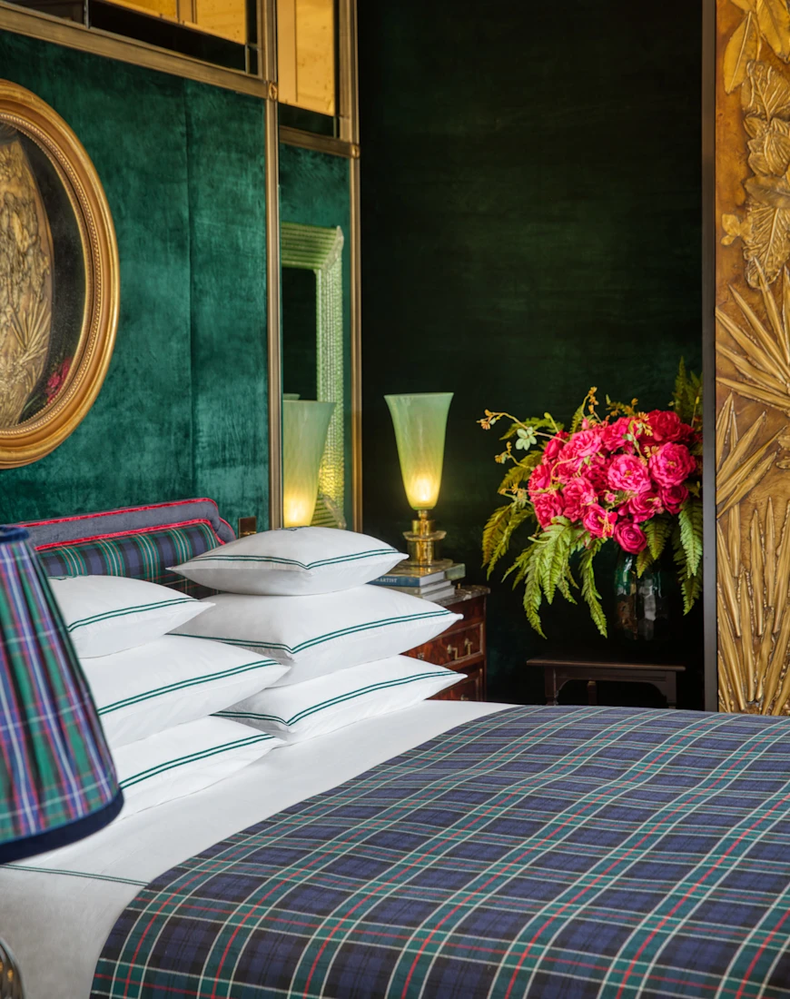 a bed with a green plaid blanket near a vase of red flowers