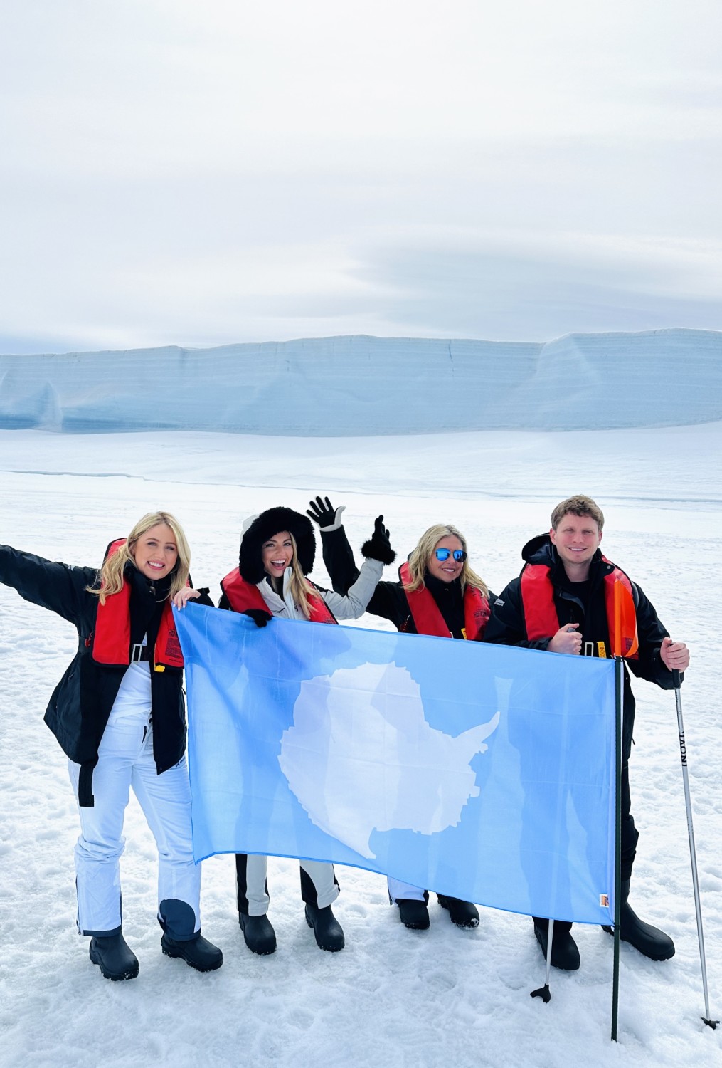 A group of people on ice holding up a blue flag and posing for a photo