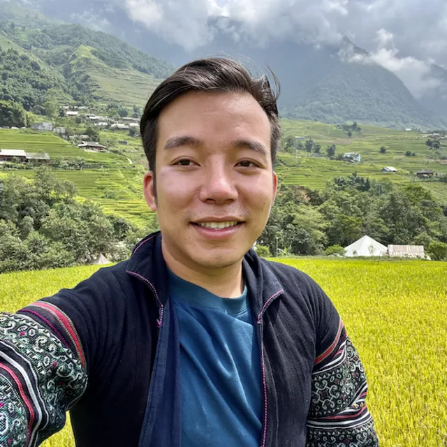 Travel advisor Jacob Nguyen in a blue shirt smiling in front of a green field