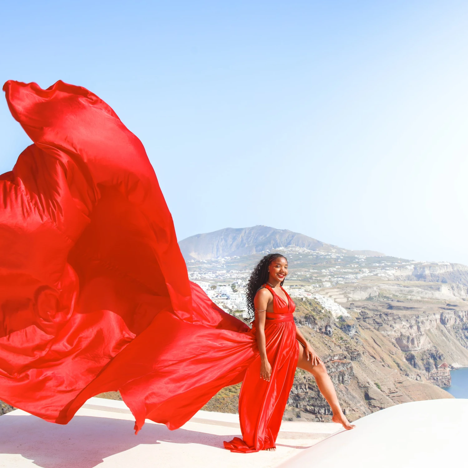 Travel advisor posing in red dress beside a sea 