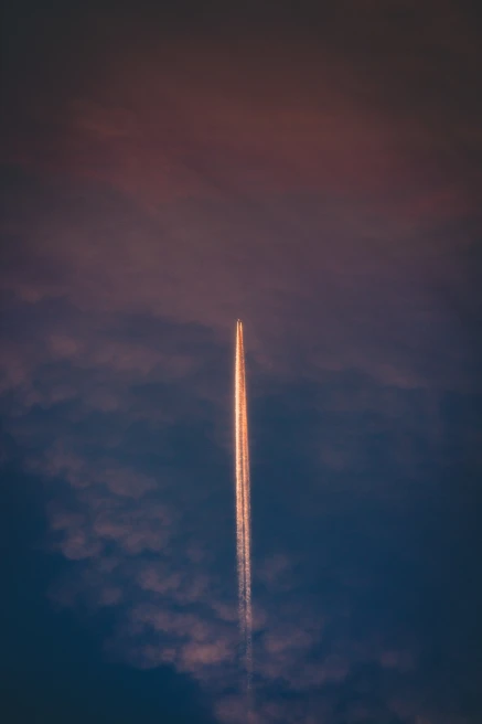A plane flying in a pink and blue sky with a jet stream.
