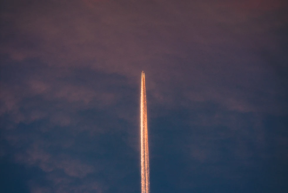 A plane flying in a pink and blue sky with a jet stream.