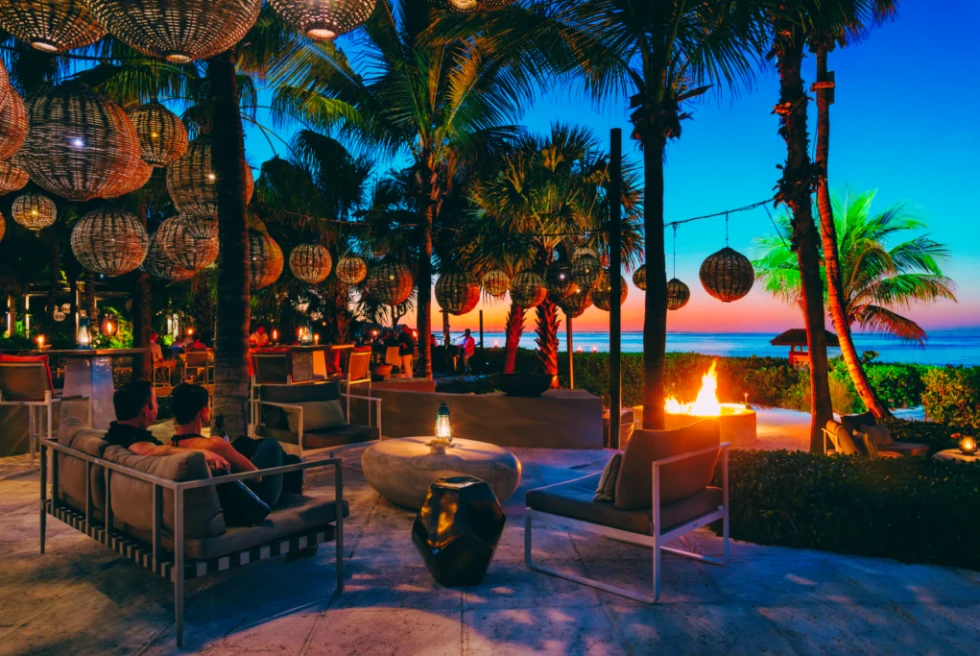 An island restaurant at night with a sunset at distance and a fire pit. 